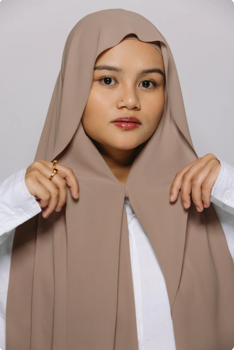 Woman wearing a beige hijab against a plain background