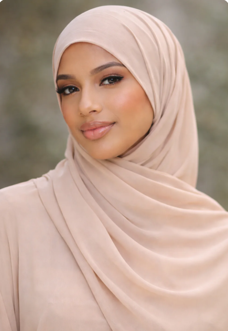 Woman wearing a beige hijab against a blurred natural background