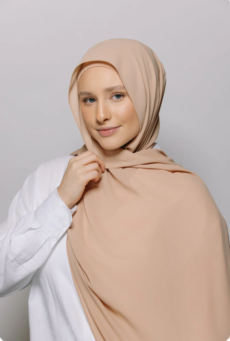 Woman wearing a beige hijab against a plain background