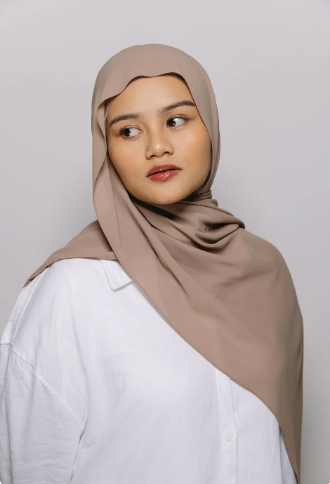 Woman wearing a beige hijab and white shirt against a light gray background