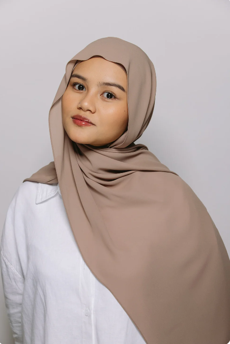 Woman wearing a beige hijab against a plain background