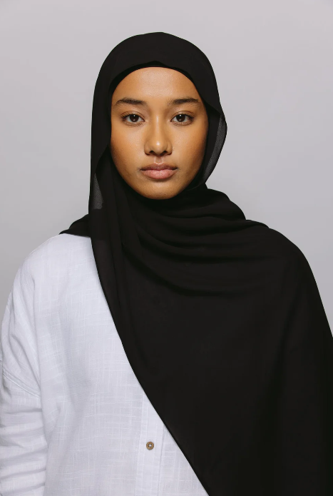 Woman wearing a black hijab and white shirt against a gray background