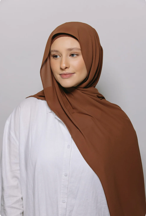 Woman wearing a brown hijab and white shirt against a plain background