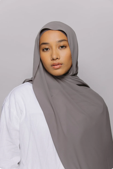 Woman wearing a gray hijab and white shirt against a plain background