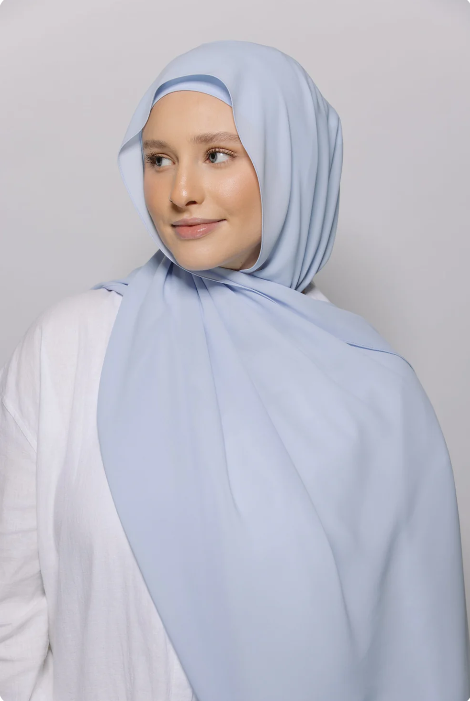 Woman wearing a light blue hijab against a plain background