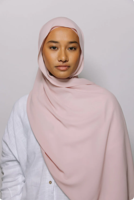 Woman wearing a light pink hijab against a plain background