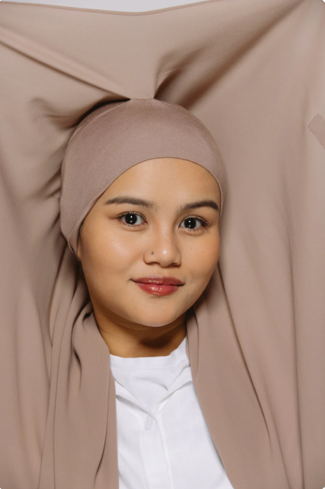 Woman wearing a beige hijab with a plain background